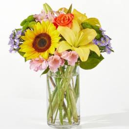 Bouquet of sunflowers, lilies, roses, and pink flowers in a glass vase