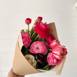 Handheld bouquet of pink and red ranunculus wrapped in kraft paper