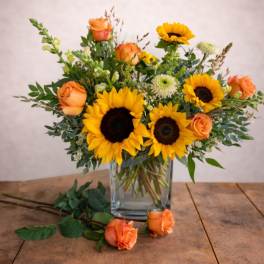 Sunflowers and orange roses arranged in a clear glass vase