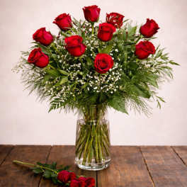 Red roses arranged in a clear glass vase with a single rose on the table