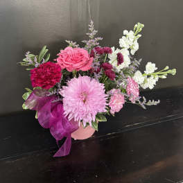 Low pink and white mixed flower arrangement in a pink vase with a purple ribbon bow