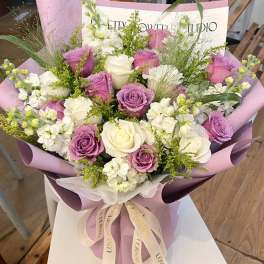 Bouquet of white and lavender roses wrapped in purple paper
