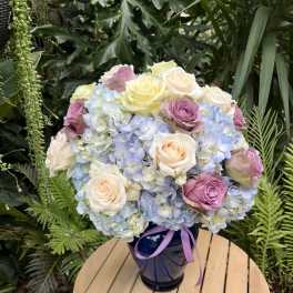 Bouquet of pastel roses and blue hydrangeas in a dark vase