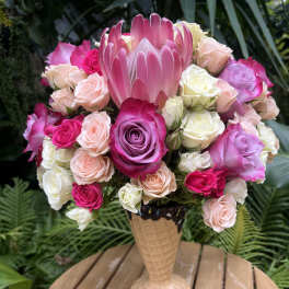 Pink and white roses arranged in a tall vase with a large pink protea