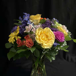 Mixed bouquet of roses, daisies, and purple flowers in a glass vase