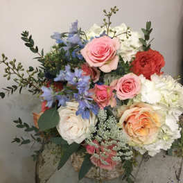 Mixed bouquet of roses, hydrangeas, and blue flowers in a container