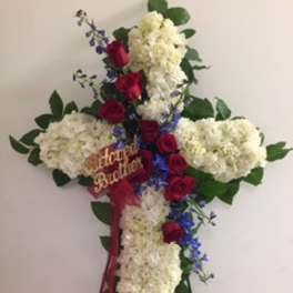 Cross-shaped floral tribute with white hydrangeas, red roses, and blue flowers