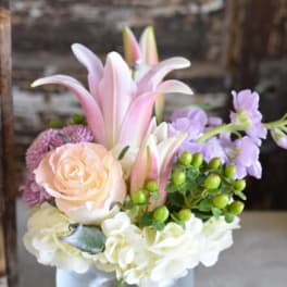 Pink lilies and roses arranged in a glass vase with white blooms