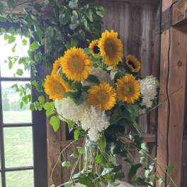 Sunflowers and white hydrangeas in a glass vase with trailing greenery