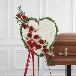 Heart-shaped white floral spray with red roses beside a casket