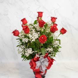 Red roses arranged in a glass vase with white baby's breath and ribbon