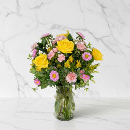 Mixed bouquet of yellow roses and pink flowers in a clear glass vase with a ribbon bow