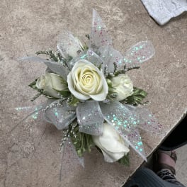 Small corsage of white roses with iridescent glitter ribbon on a work surface