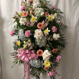 Standing floral spray with pink, white, and yellow blooms and a pink ribbon