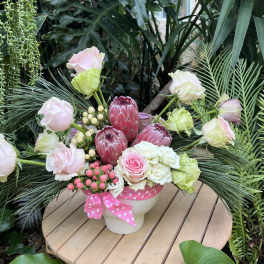 Pink and white floral arrangement in a white pot with a pink ribbon