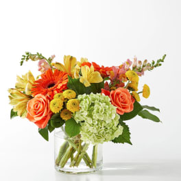 Mixed bouquet of orange, yellow, and green flowers in a clear glass vase
