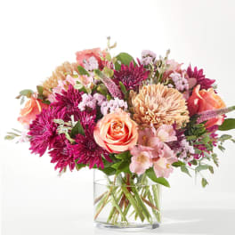 Mixed bouquet of pink, peach, and purple flowers in a clear glass vase