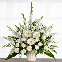 Tall white arrangement of roses, gerbera daisies, and other blooms in a ribbed white pot