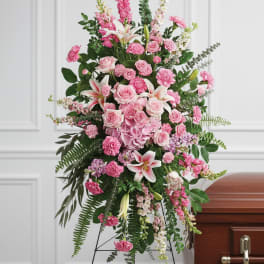 Tall standing spray of pink roses, lilies, and carnations on an easel beside a casket