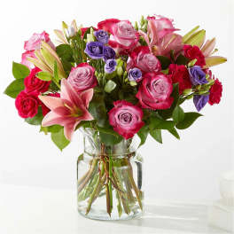 Bouquet of pink and purple roses with lilies in a clear glass vase