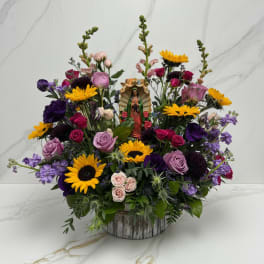 Colorful mixed flower arrangement with a small religious figurine in a rustic container