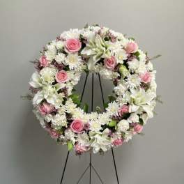 Circular floral wreath with pink roses and white blooms on a black stand