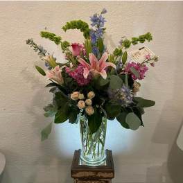 Tall mixed bouquet with pink lilies, roses, and blue flowers in a glass vase