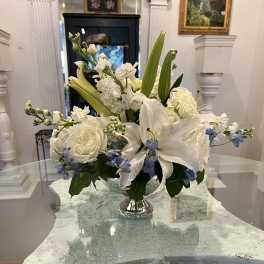 Low white and blue flower arrangement with lilies and roses in a silver pedestal vase