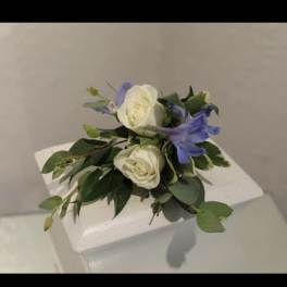 Small cluster of white roses and blue flowers arranged on a white pedestal.