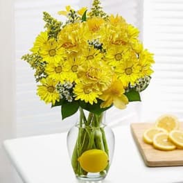 Yellow flower bouquet in a clear glass vase with a lemon inside