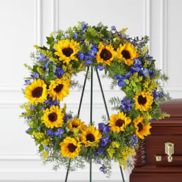 Sunflower and blue floral wreath on a stand beside a casket