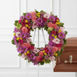 Colorful floral funeral wreath on a white stand beside a casket