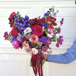 Handheld bouquet of pink, red, and purple flowers tied with a burgundy ribbon.