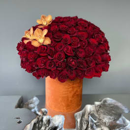 Red rose arrangement in an orange velvet vase with peach orchids