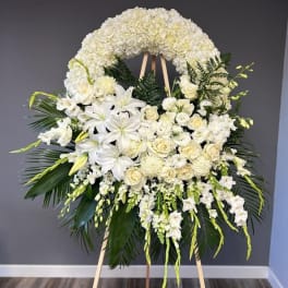 Large white funeral wreath on an easel with lilies and roses