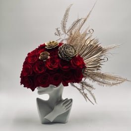 Red rose arrangement in a gray sculptural vase with gold dried accents