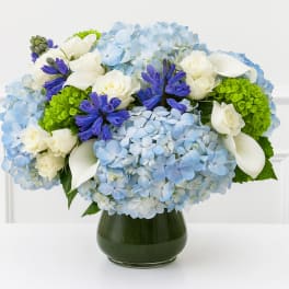 Blue hydrangeas with white roses and purple flowers in a dark glass vase