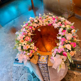 Large circular floral wreath in pink, peach, and white around a copper basin