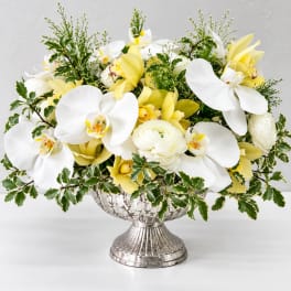 White orchids and yellow blooms in a silver pedestal vase