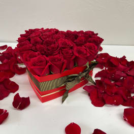 Red roses arranged in a heart-shaped gift box with scattered petals