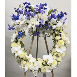Large floral wreath on an easel with white orchids, blue flowers, and pale blooms