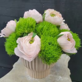 Pale pink flowers arranged in a ribbed white vase with bright green filler