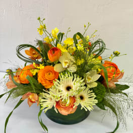 Orange and white mixed flower arrangement in a low green vase