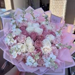 Pink and white rose bouquet with small white blossoms wrapped in pink paper