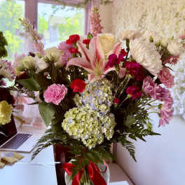 Mixed bouquet of pink and white flowers in a glass vase with a red ribbon