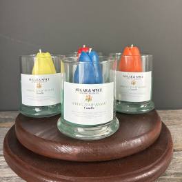Set of glass jar candles with colorful tulip-shaped wax on a round wooden stand.