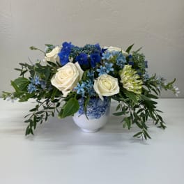 White roses and blue flowers arranged in a blue-and-white vase