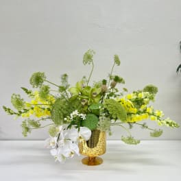 Green and white floral arrangement in a gold speckled vase