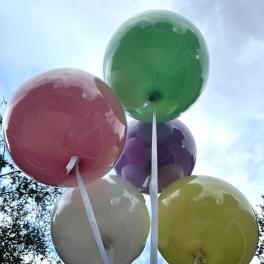 Cluster of colorful balloons with white ribbons against the sky
