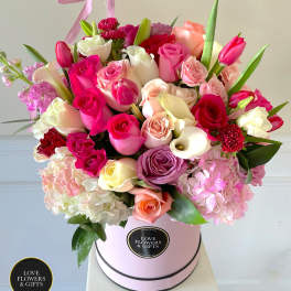 Round hatbox arrangement of mixed pink, white, and peach roses with tulips and calla lilies.